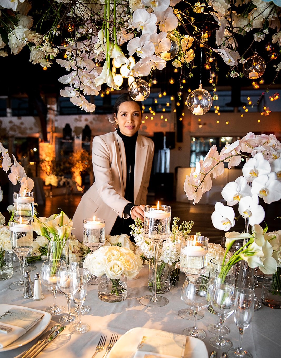 Tara Manchanda beneath an orchid installation and candlelit tablescape at a wedding she planned