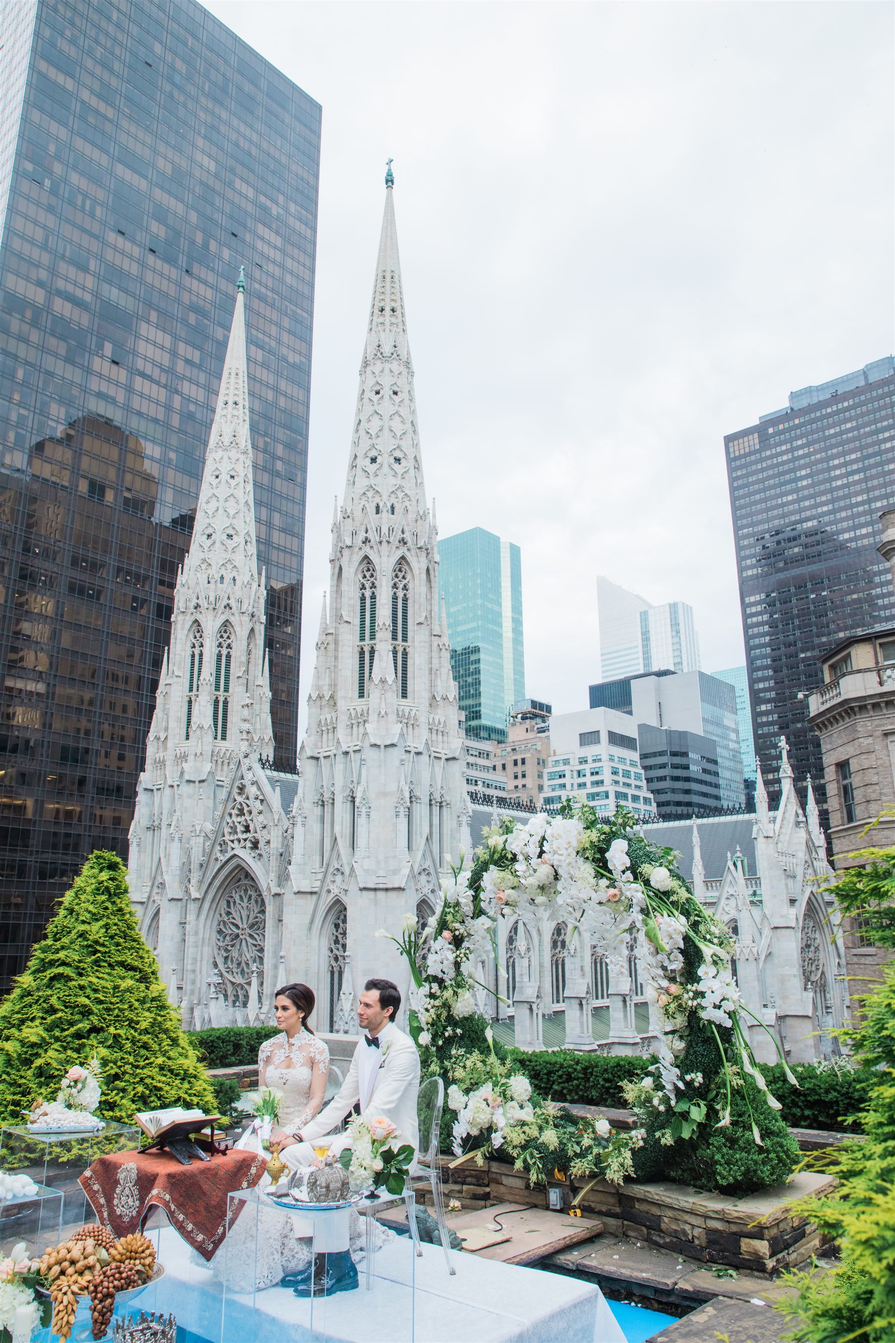The groom waits at a white floral arch, St. Patrick's Cathedral beyond